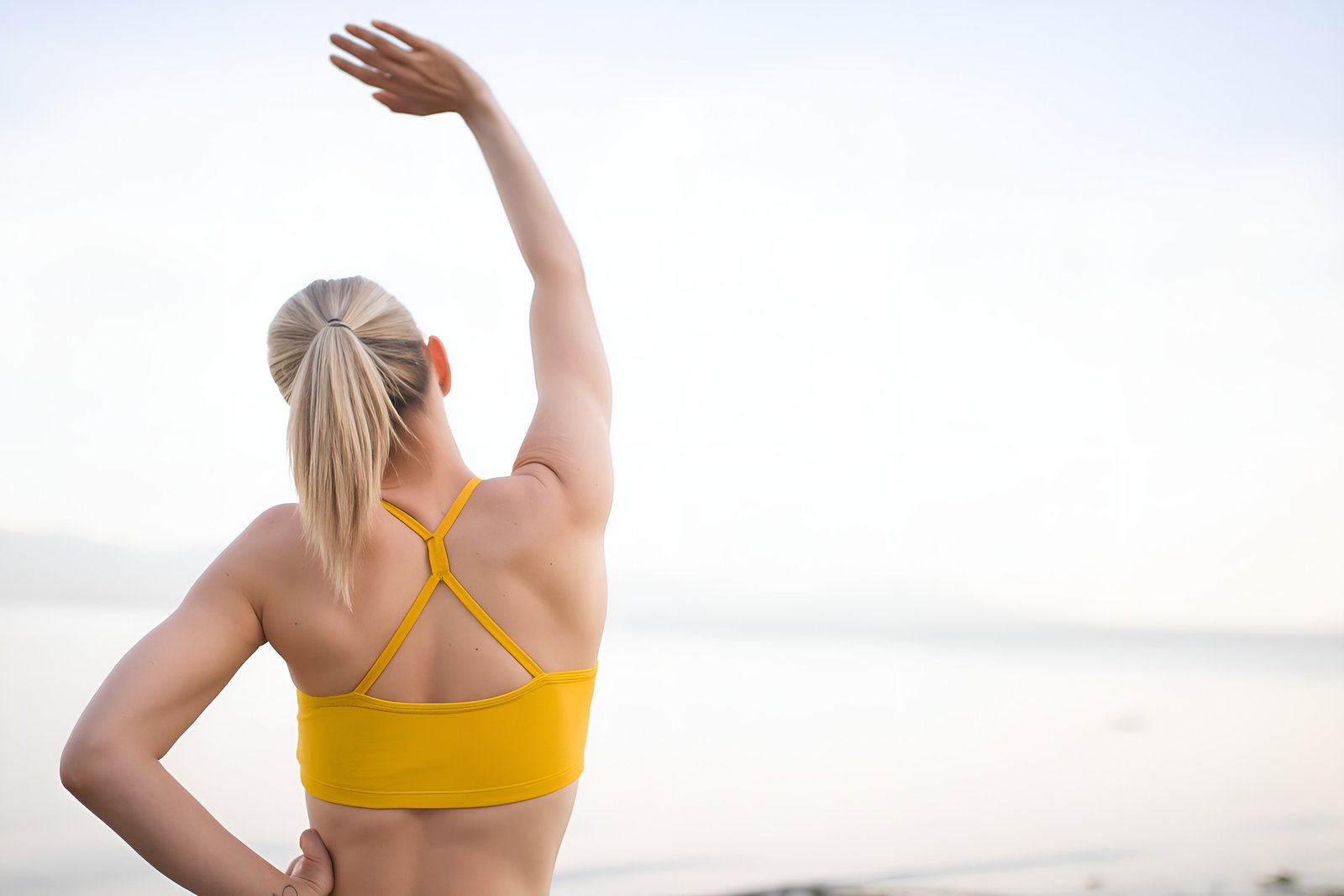 Rear View of Woman Stretching Outdoors in Yellow Sportswear by the Sea